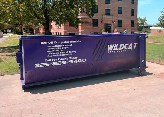 Purple Wildcat Site Services roll-off dumpster beside a brick building