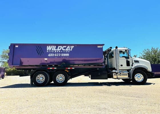 Wildcat Site Services truck carrying a branded purple roll-off dumpster